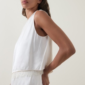 Model wearing Vince Asymmetric Lace Trim Top in cream, sleeveless with round neckline, paired with matching cream wide-leg trousers.