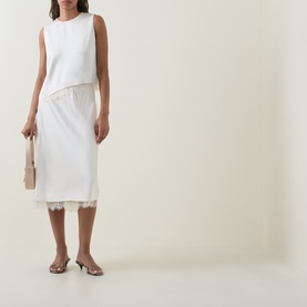 Model wearing Vince Asymmetric Lace Trim Top in cream, styled with a white midi skirt with lace hem, neutral slides and a small clutch bag.
