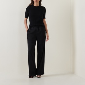 Model wearing Vince black wool-cashmere short sleeve top, styled with wide-leg black trousers and black heeled sandals.