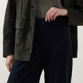 Model wearing Vince navy trousers in a relaxed wide-leg fit, styled with a dark olive suede jacket and grey top.