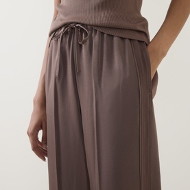 Model wearing Vince taupe haze trousers with drawstring waistband and side pockets, styled with a ribbed vest top