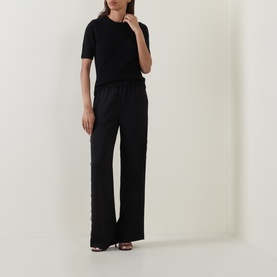 Model wearing Vince black wide-leg trousers with elasticated waist, styled with a black short-sleeve top and strappy sandals.