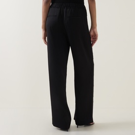 Model wearing Vince black wide-leg trousers with elasticated waistband, shown from behind, styled with black heeled sandals.