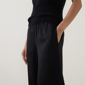 Model wearing Vince black wide-leg trousers with elasticated waist, styled with a black ribbed knit top, hands in pockets.