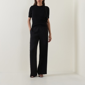 Model wearing Vince black wide-leg trousers with elasticated waist, styled with a black short-sleeve top and strappy heels.