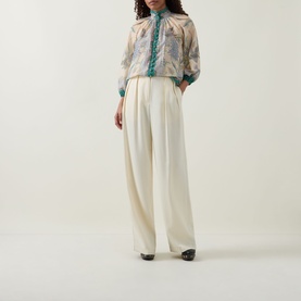 Model wearing Zimmermann Indra Billow Scarf Floral Blouse in Cream Scarf Floral with wide-leg cream trousers and black heeled boots.