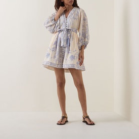 Model wearing Zimmermann dress in Cream Lilac Floral, featuring blouson sleeves, lace trim, and belted waist, styled with gold strappy sandals.