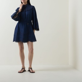 Model wearing Zimmermann ink blue mini dress with broderie anglaise hem, bell sleeves, and drawstring waist, styled with tan flat sandals