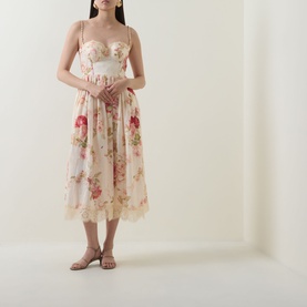 Model wearing a cream floral midi dress with lace trim, structured bodice, and spaghetti straps, styled with strappy flat sandals