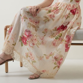Model wearing cream floral maxi skirt with pink rose print and lace hem detail, styled with strappy flat sandals