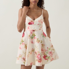 Model wearing Zimmermann Roselight Rose Floral Mini Dress in cream with pink rose print, V-neckline, narrow straps and flared skirt. Gold necklace