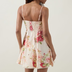 Model wearing Zimmermann Roselight Rose Floral Mini Dress in cream, showing rear smocked detailing, adjustable straps, and flared lace-trimmed skirt.