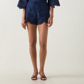 Model wearing Zimmermann blue cotton broderie anglaise shorts with scalloped hem, styled with matching top and brown mule heels.