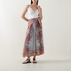 Model wearing Zimmermann Blue Paisley Floral silk skirt with wrap-style tie, styled with white lace cami top and black flat sandals.