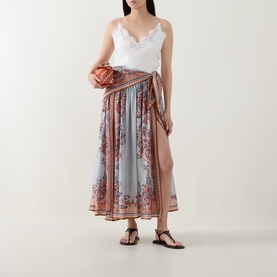 Model wearing Zimmermann silk skirt in Blue Paisley Floral, styled with white lace cami, brown sandals, and small woven clutch bag.