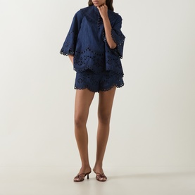 Model wearing Zimmermann blue cotton broderie anglaise top with flare sleeves, styled with matching navy shorts and tan heeled mules.