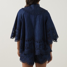 Model wearing Zimmermann blue cotton broderie anglaise top with flared sleeves and scalloped hem, styled with matching shorts, back view.