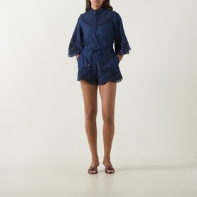 Model wearing Zimmermann blue cotton broderie anglaise playsuit with belted waist, flared sleeves, and scalloped hem, styled with brown sandals