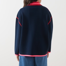Model wearing Essentiel Antwerp navy cardigan, back view, with pink contrast trim detailing and blue denim jeans.