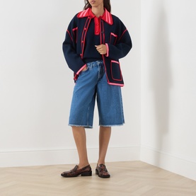 Model wearing Essentiel Antwerp navy cardigan with red contrast trim and pockets, styled with blue denim shorts and brown loafers.