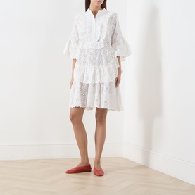 Model wearing Essentiel Antwerp white cotton broderie dress with tiered skirt and flared sleeves, styled with red ballet flats.