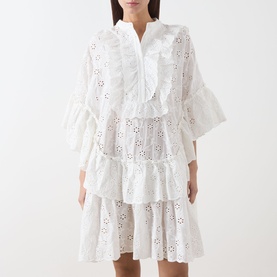 Model wearing Essentiel Antwerp white cotton broderie anglaise mini dress with tiered ruffle layers and flared sleeves.