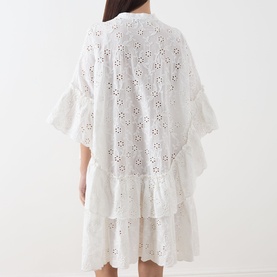 Model wearing Essentiel Antwerp white cotton broderie anglaise dress, back view, showing tiered ruffle hem and flutter sleeves.