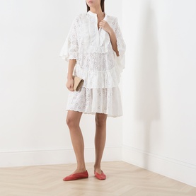 Model wearing Essentiel Antwerp white cotton broderie dress with tiered ruffle skirt, styled with red flat shoes and a small clutch bag.
