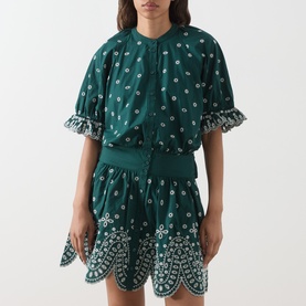 Model wearing Essentiel Antwerp Bottle Green cotton mini dress with white floral embroidery, ruffle hem and elasticated waist