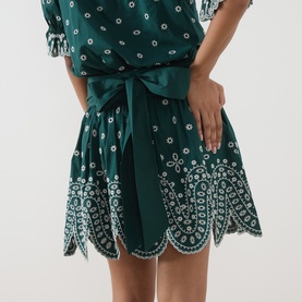 Model wearing Essentiel Antwerp bottle green cotton dress with white floral eyelet embroidery, scalloped hem, and satin tie waist.