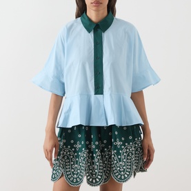 Model wearing Essentiel Antwerp aquamarine cotton shirt with green collar, peplum hem, styled with green embroidered mini skirt.