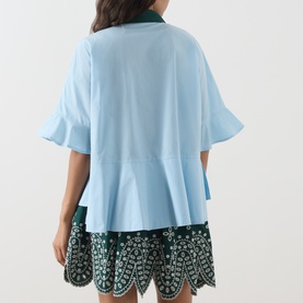 Model wearing Essentiel Antwerp aquamarine cotton shirt, back view, fluted sleeves and peplum hem, styled with dark floral embroidered shorts.
