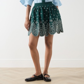 Model wearing Essentiel Antwerp bottle green cotton mini skirt with white floral embroidery and scalloped hem, styled with black loafers