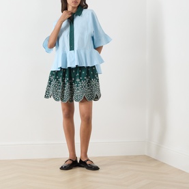 Model wearing Essentiel Antwerp bottle green cotton broderie anglaise mini skirt, styled with a light blue tiered top and black Mary Jane flats.