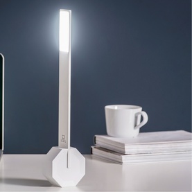 Gingko Desk Light in white with illuminated LED strip and octagonal base, styled on a desk with stacked magazines and a coffee cup