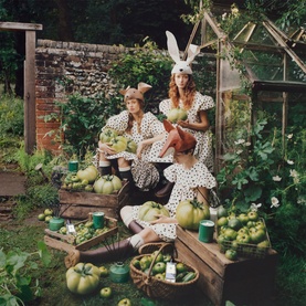 Jo Malone Green Tomato Vine Candle lifestyle shot with two models in bunny ears and polka dot dresses among tomato plants and garden produce.