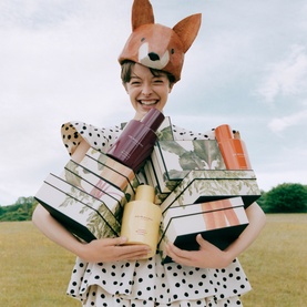 Model with Jo Malone Veggies Travel Cologne Trio fragrance gift set, holding stacked boxes, wearing polka dot dress and fox hat