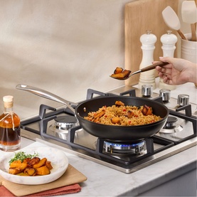 Le Creuset Toughened Non-Stick Deep Frying Pan 26cm on gas hob, cooking rice dish, with cast stainless steel riveted handle. Styled kitchen setting.