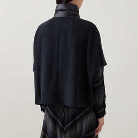 Model wearing Luisa Cerano anthracite knit cape, back view, with leather-trim collar and lace sleeve detail, styled with chevron-print skirt.