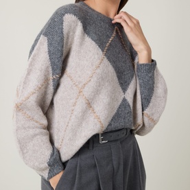 Model wearing Luisa Cerano multi-coloured argyle knit jumper in grey and beige, styled with grey tailored trousers and belt.