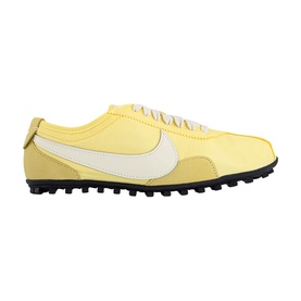 Nike trainer in soft yellow with cream swoosh, suede toe cap, and black multi-stud sole. Low-profile lace-up silhouette.