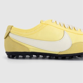 Nike trainer in soft yellow with cream Swoosh logo, black rubber outsole, lace-up front, close-up detail shot