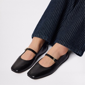 Model wearing Whistles Mary Jane Ballet Flats in black leather with gold buckle strap, styled with navy pinstripe wide-leg trousers.
