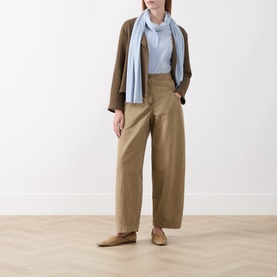 Model wearing Masai Slate Black cardigan with wide-leg tan trousers, light blue shirt and scarf, styled with tan flat shoes.