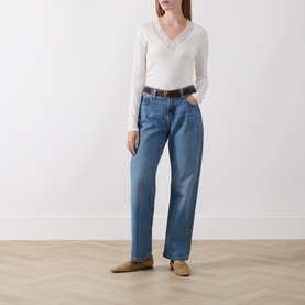 Model wearing Masai cream long-sleeve top with henley neckline, styled with blue straight-leg jeans and a brown belt.