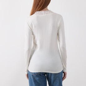 Model wearing Masai cream long-sleeve top, rear view, with delicate lace trim at shoulder and neckline. Styled with blue jeans.