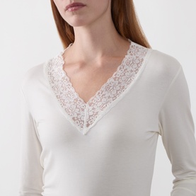 Model wearing Masai cream long-sleeve top with V-neck and floral lace trim detail at neckline.
