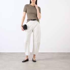 Model wearing Nili Lotan vintage cream wide-leg trousers with patch detailing, styled with a khaki tee, black ballet flats, and clutch bag.