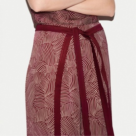 Model wearing Jigsaw red womenswear dress with abstract wave print, featuring tied wrap detail at waist