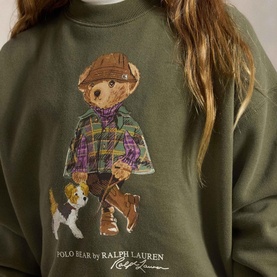 Model wearing Ralph Lauren Polo Bear Logo Fleece Sweatshirt in Cruise Olive with Polo Bear and dog graphic on back.